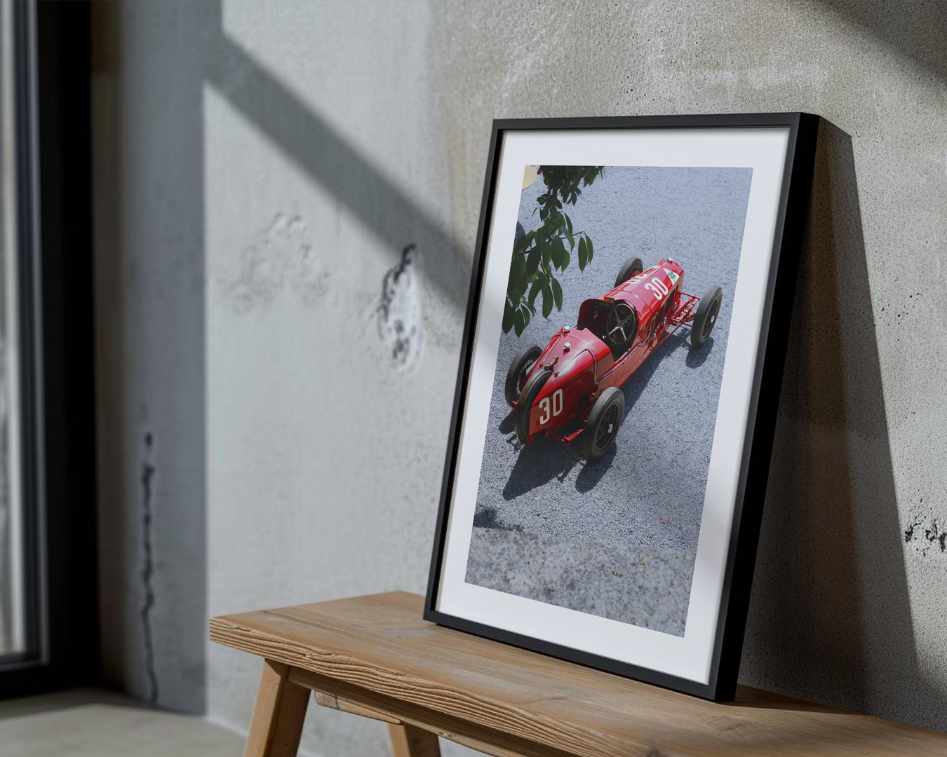 A framed photograph of a vintage red race car with the number "30," leaning against a grey wall on a wooden surface.